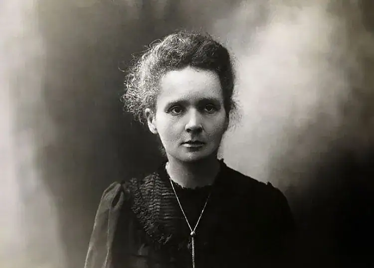 Retrato em preto e branco de uma mulher com cabelo encaracolado e expressão séria, vestida com roupa antiga e colar, olhando para a câmera.